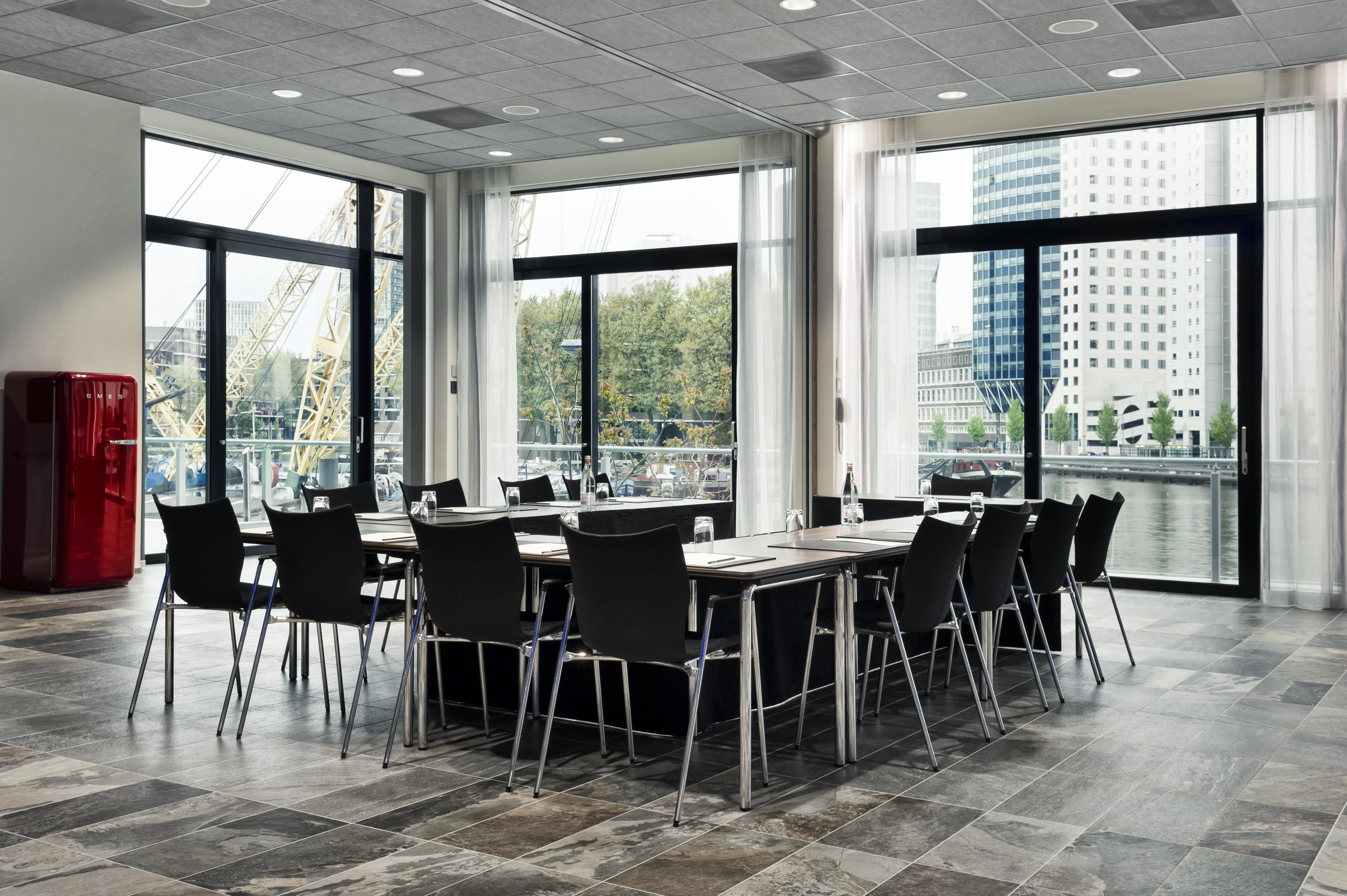 Mainport Hotel Rotterdam, A Hilton Affiliate Hotel Exterior foto The photo shows a modern meeting room with large windows allowing natural light to flood in. Inside, there is a long rectangular table surrounded by several sleek black chairs. The flooring appears to be tiled with a contemporary design. In the backg